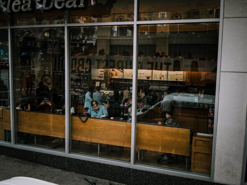 People sitting inside a glass-front café with wooden benches and reflections on the windows