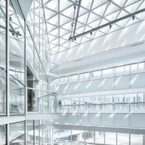 Bright modern atrium with glass walls, white steel beams, and skylight ceiling in a minimalist building
