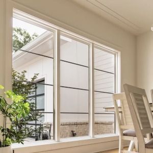 Bright sunroom with large windows, potted plant, and white chairs overlooking a courtyard
