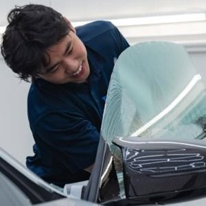 Person smiling while cleaning a car windshield with a cloth
