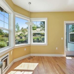 Bright empty room with bay windows, yellow walls, hardwood floors, and sunlight streaming in