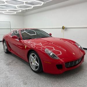 Red Ferrari sports car parked in a white garage with hexagonal ceiling lights.