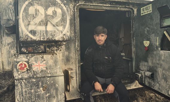 A man is sitting in the doorway of a military vehicle.