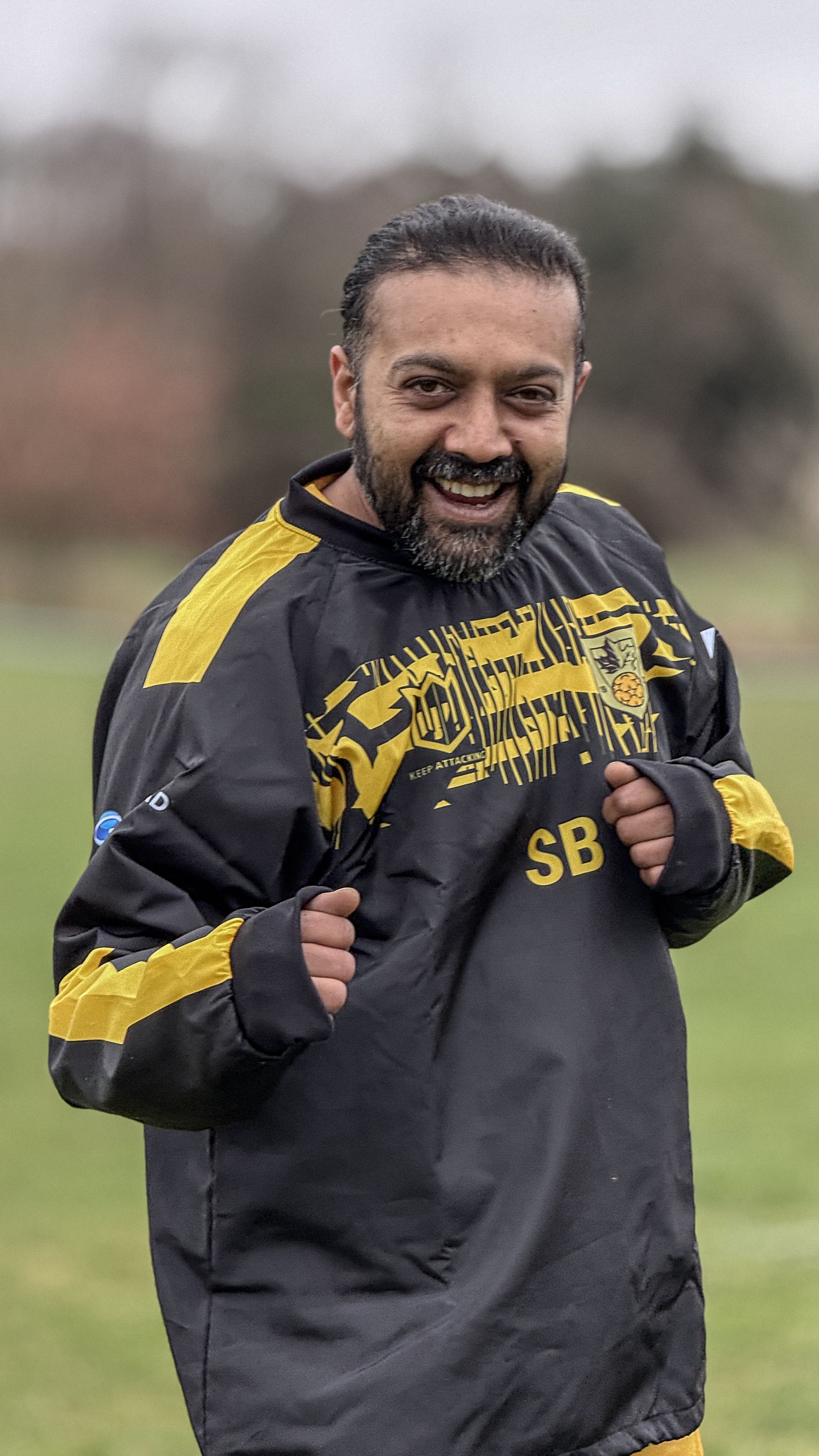 A man with a beard is wearing a black and yellow jacket and smiling.