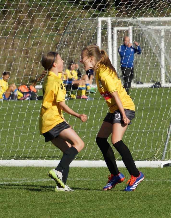 Two young girls are playing soccer on a field.