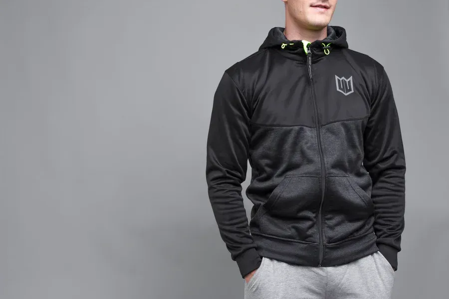 A man wearing a black hoodie and grey sweatpants is standing with his hands in his pockets.