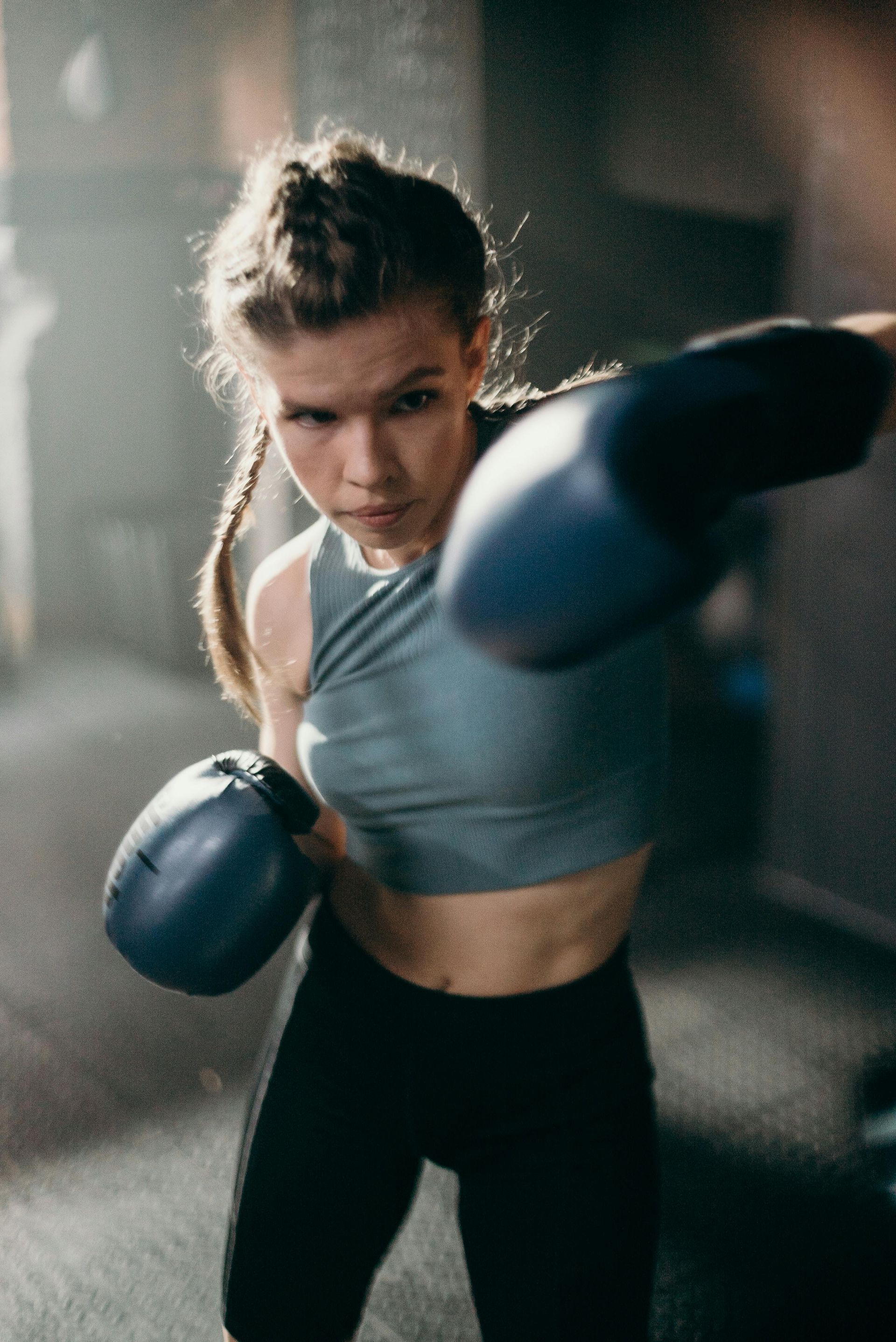 A woman is wearing blue boxing gloves in a gym.