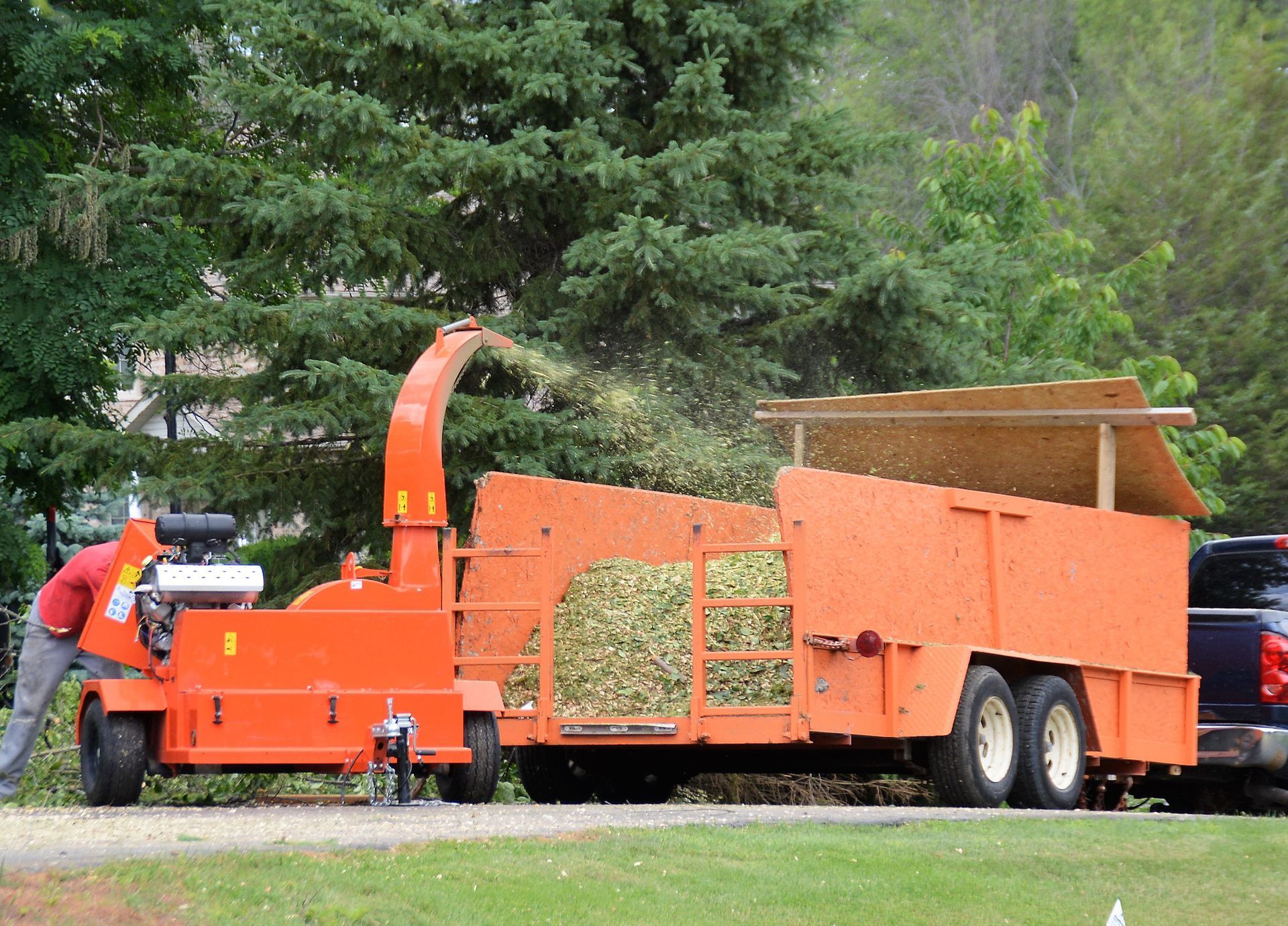 A man is pushing an orange trailer with a wood chipper attached to it.