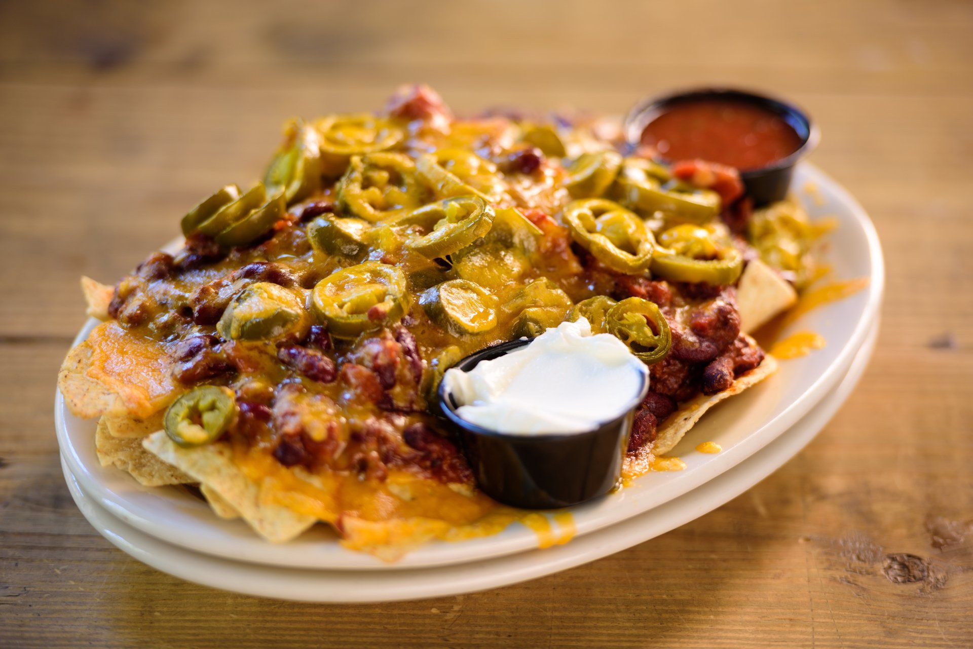 Nachos loaded with cheese, chili, jalapeños, and toppings, served with salsa and sour cream on a white plate.