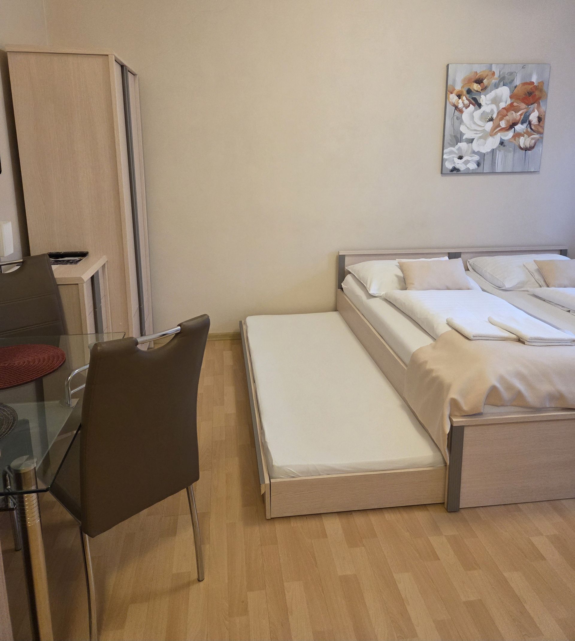 Malá hotelová izba s dvoma posteľami, rozkladacou pohovkou a kreslom na drevenej podlahe