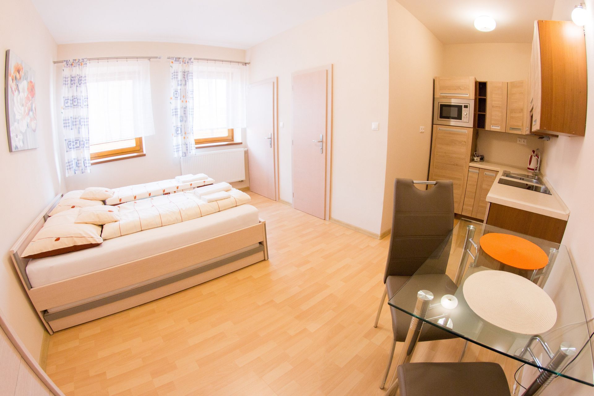 Malý štúdiový apartmán s posteľou, skleneným jedálenským stolom, kuchynským kútom a svetlými oknami