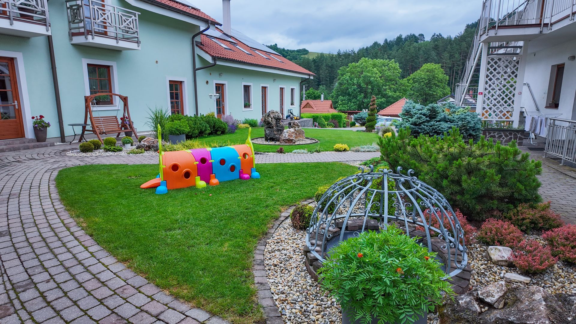 Záhradný dvor s farebnými hračkami pre zvieratá vedľa bieleho domu a kamennej cesty