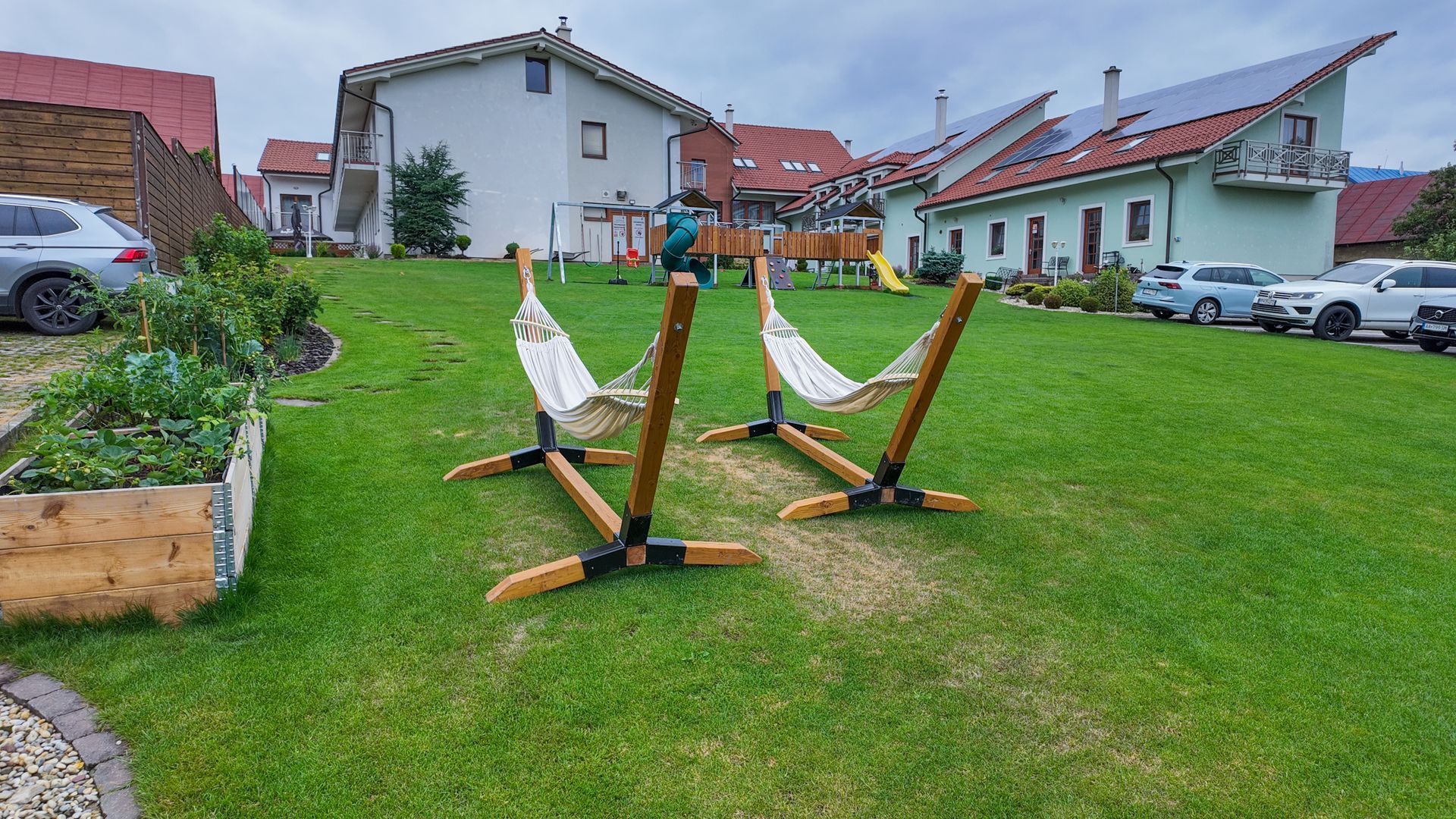 Drevené hojdačky na ihrisku na trávnatom dvore vedľa domov a zaparkovaných áut.
