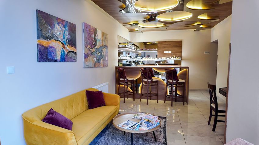Moderný lobby bar so žltou pohovkou, farebnými obrazmi, konferenčným stolíkom a jedálenským kútom v zadnej časti