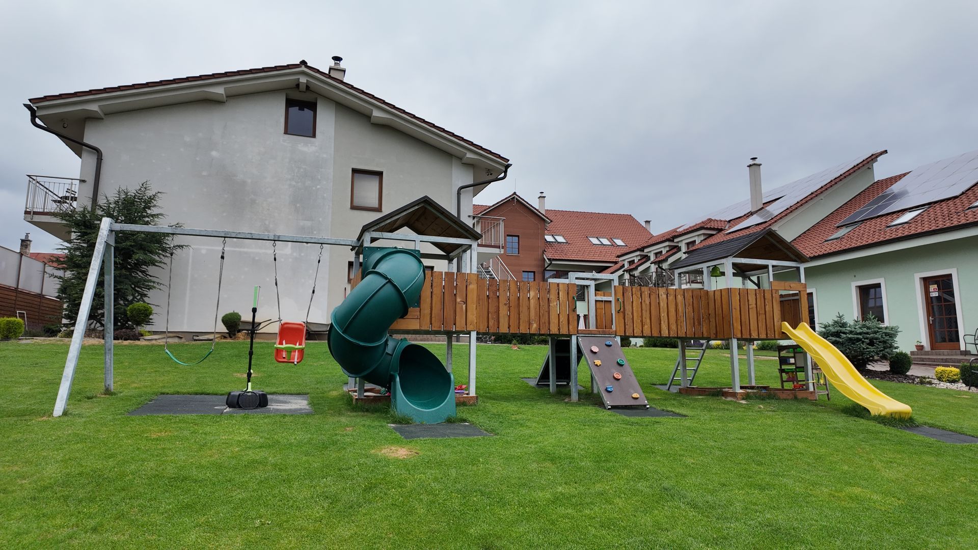 Ihrisko na dvore so zelenou šmykľavkou, hojdačkou a žltou šmykľavkou vedľa domu na trávnatom trávniku