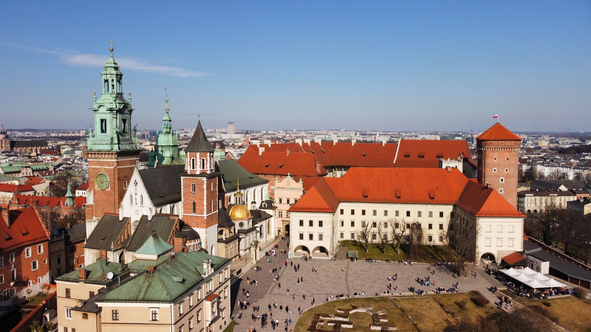 Historická panoráma mesta s budovami s červenými strechami a kostolnými vežami pod jasnou modrou oblohou