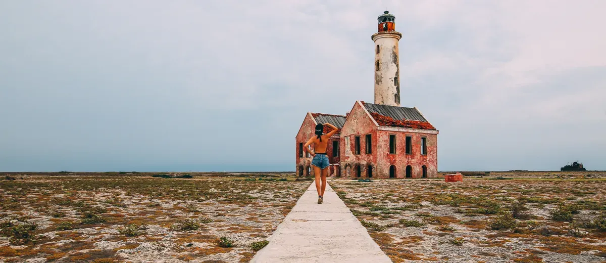 A woman is walking down a path towards a lighthouse.