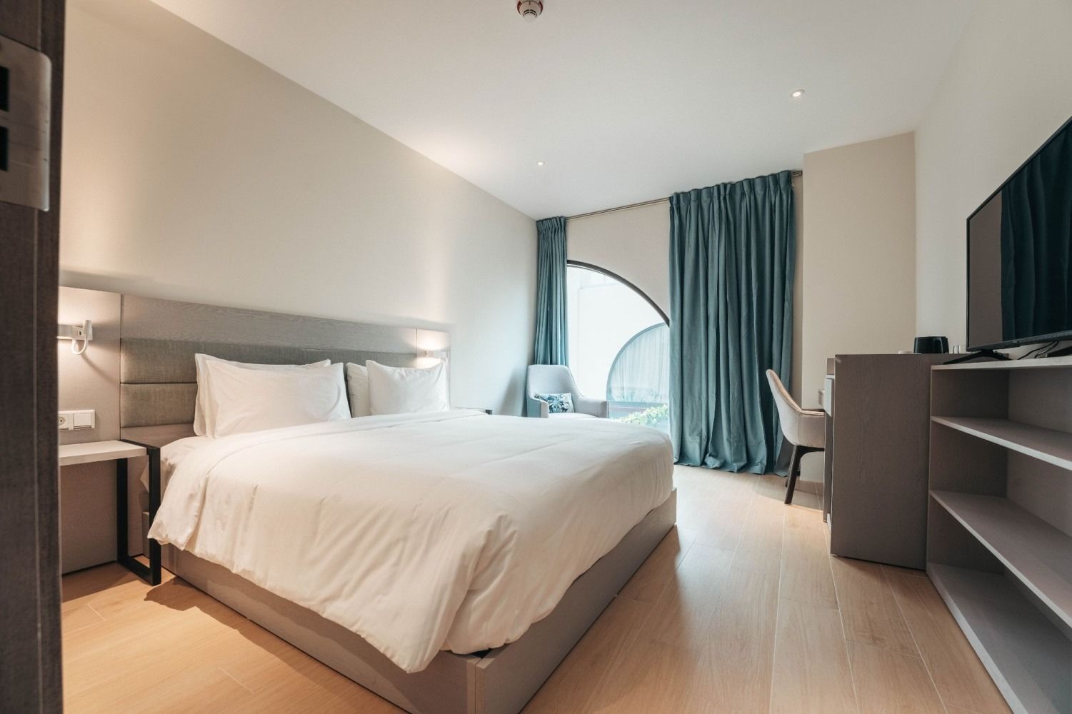A hotel room with a king size bed , desk , chair and television.