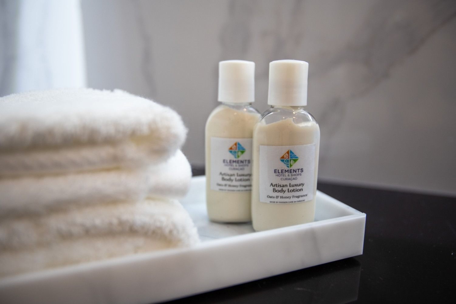 Two bottles of lotion are sitting on a tray next to a stack of towels.