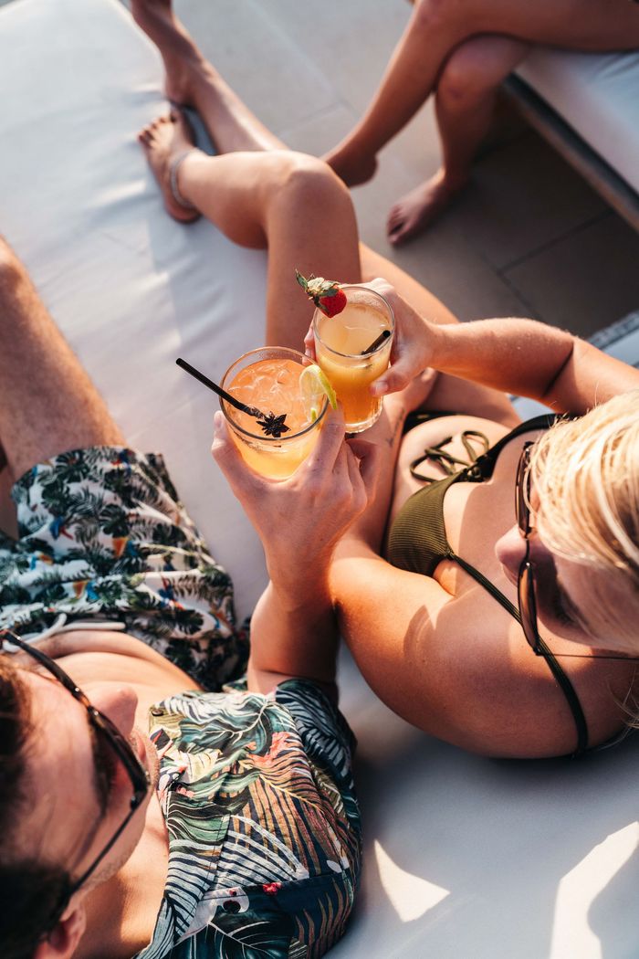 A man and a woman are laying on a couch holding drinks.