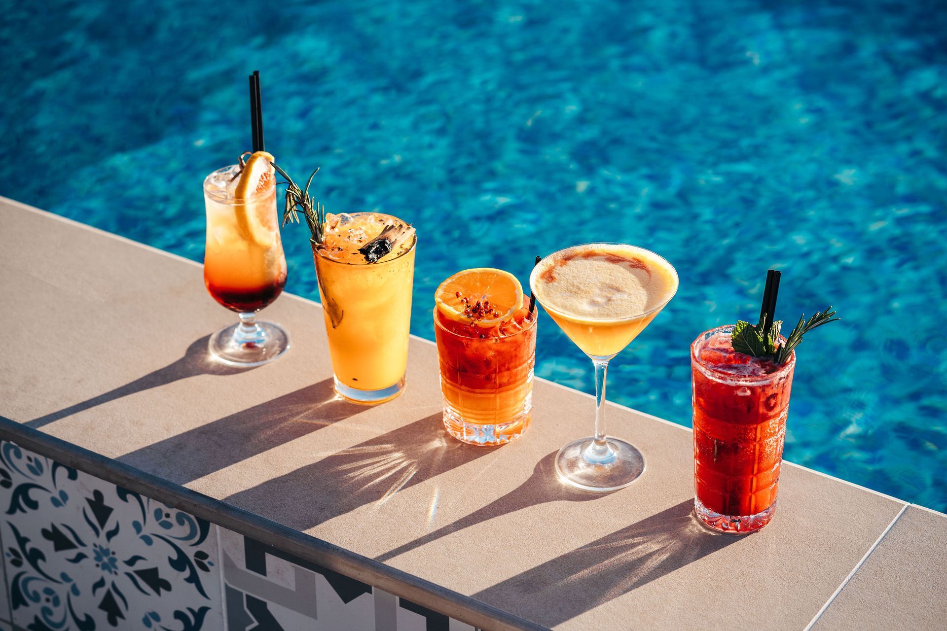 Four different types of cocktails are sitting on a table next to a swimming pool.