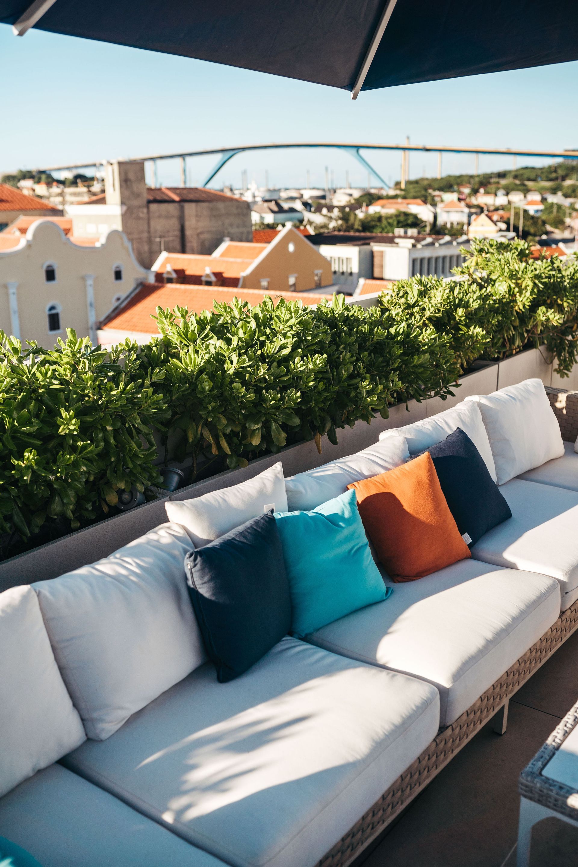 A patio with a couch and pillows under an umbrella.