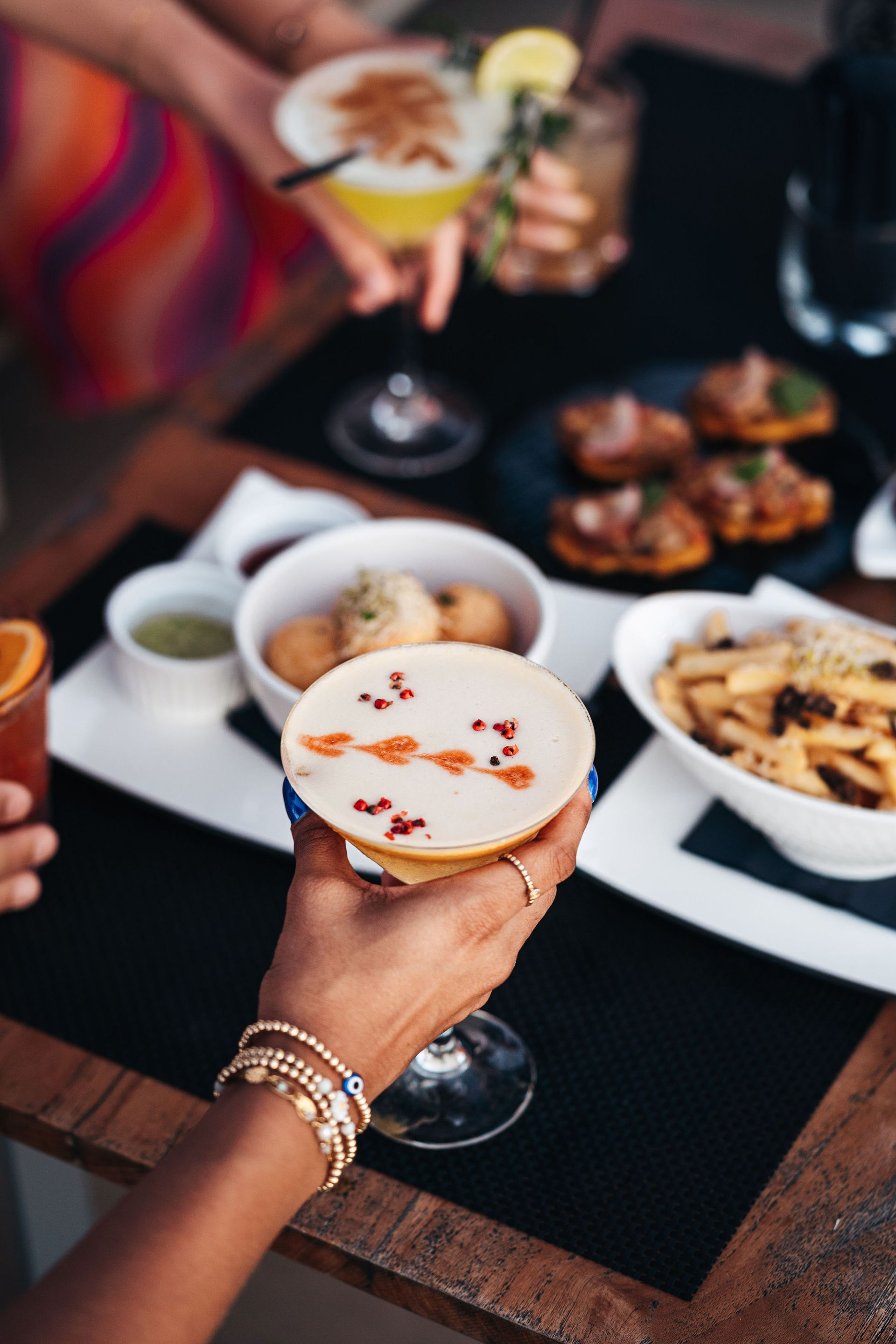 A woman is holding a drink in front of a table with food.