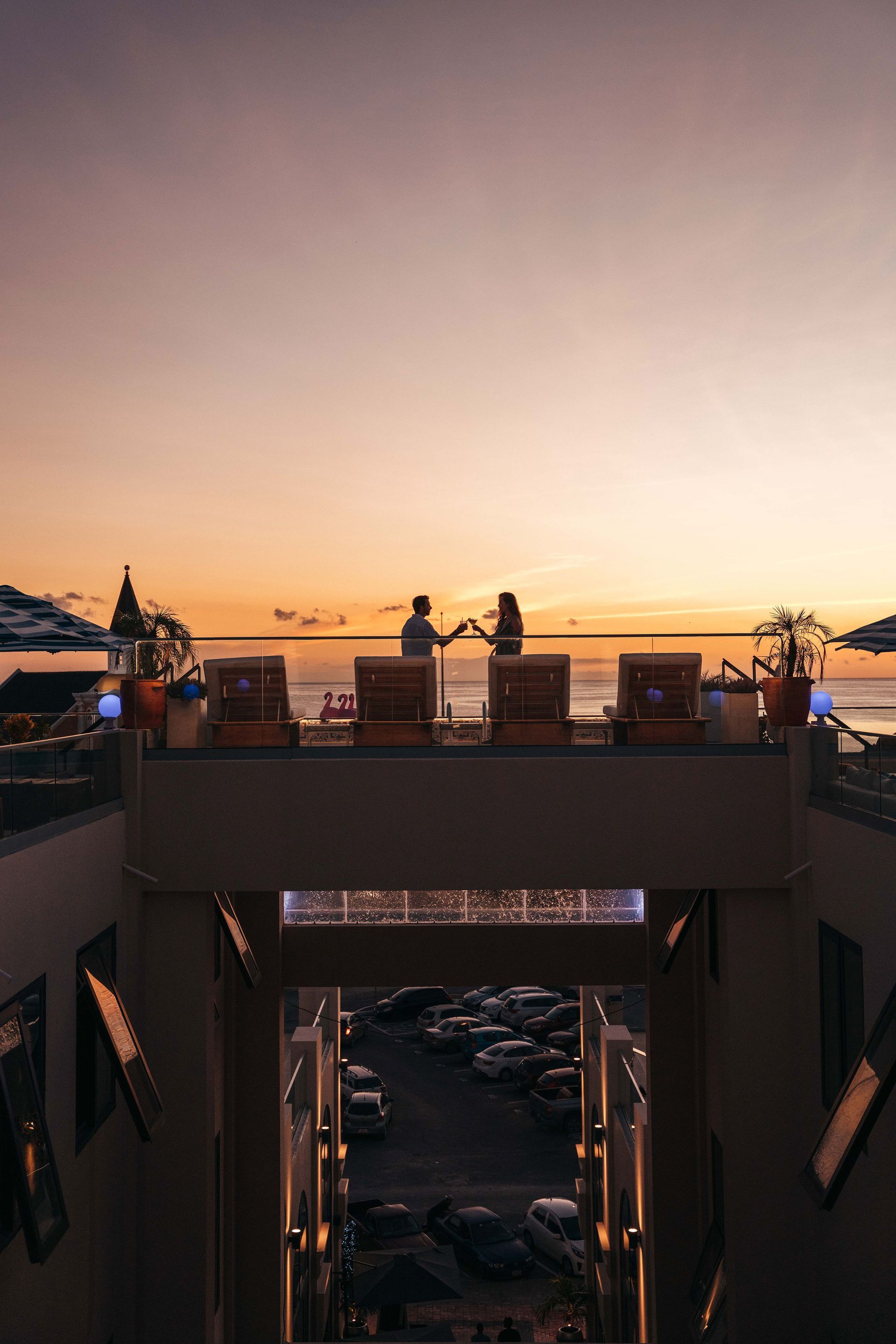 A couple is sitting on a balcony overlooking the ocean at sunset.