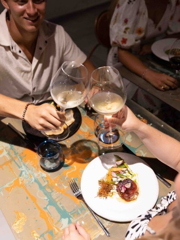 A man and a woman are sitting at a table with plates of food and glasses of wine.