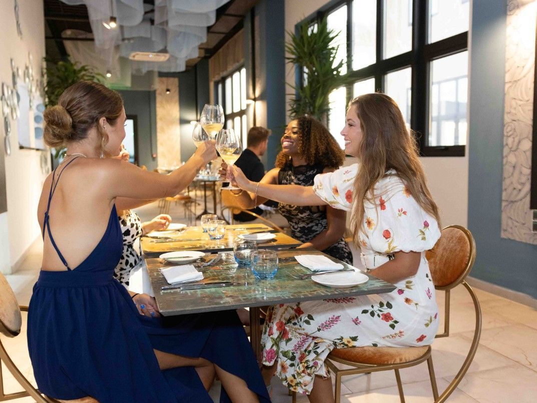 A group of women are sitting at a table in a restaurant toasting with wine glasses.