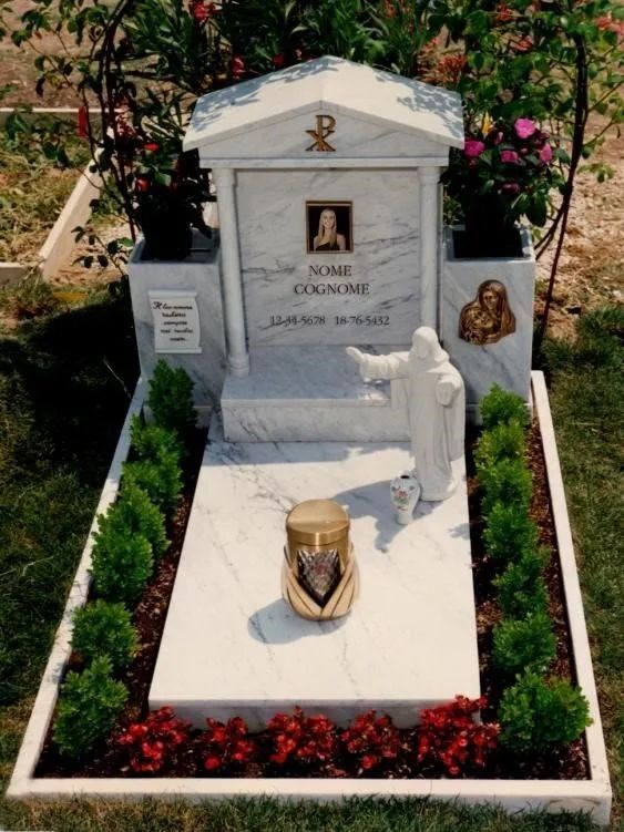Tomba commemorativa bianca con ritratto incorniciato, decorazioni floreali e fiori rossi in un'area cimiteriale ben curata.