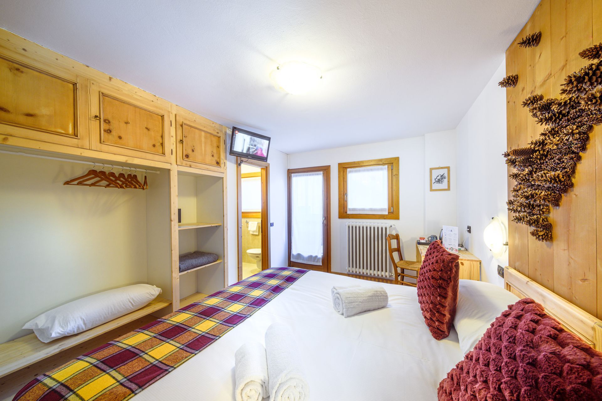 Camera da letto luminosa con due letti singoli, armadi in legno, pareti bianche e una finestra accanto al termosifone.