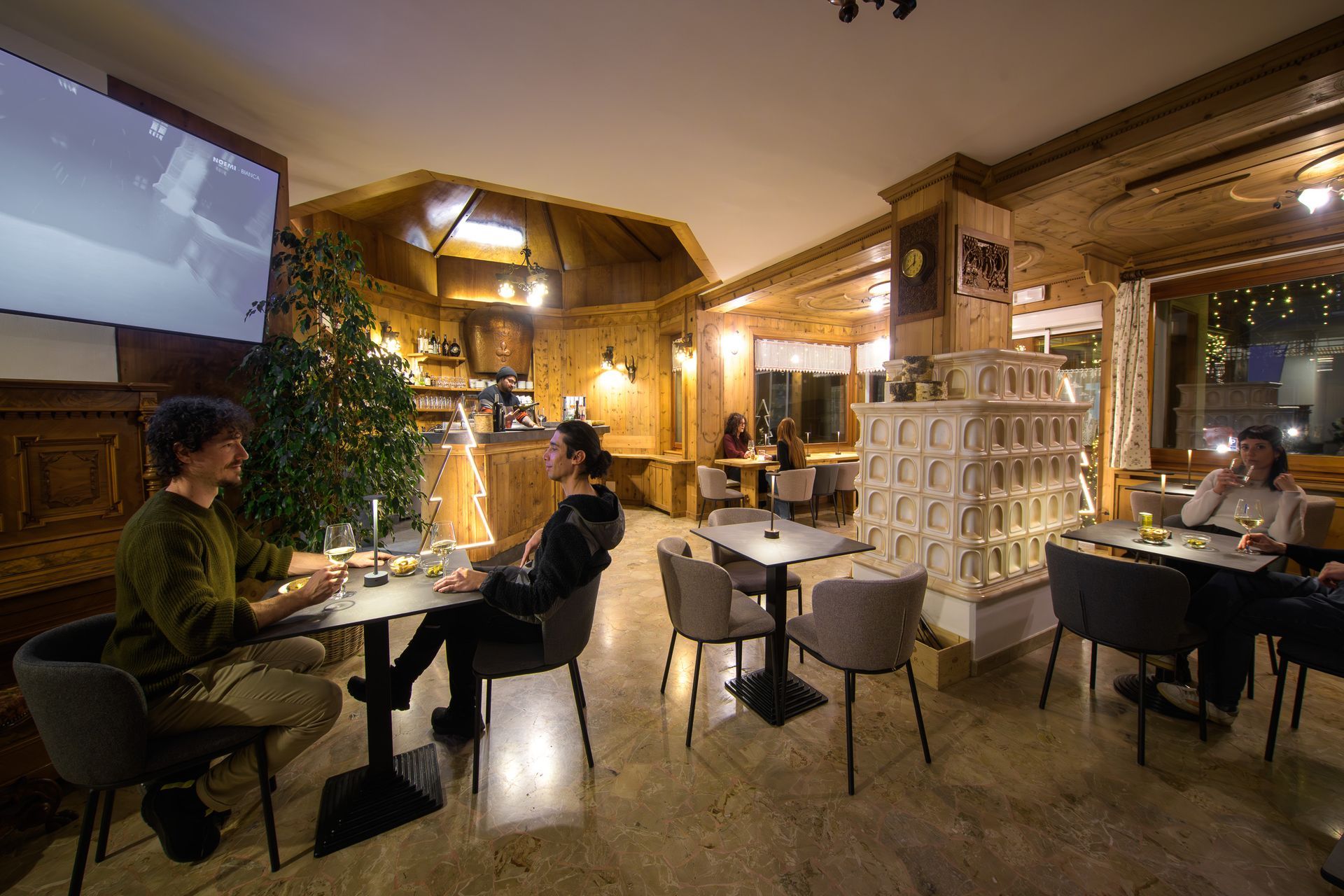 Accogliente interno del caffè con clienti seduti a tavolini sotto luci calde e decorazioni in legno.