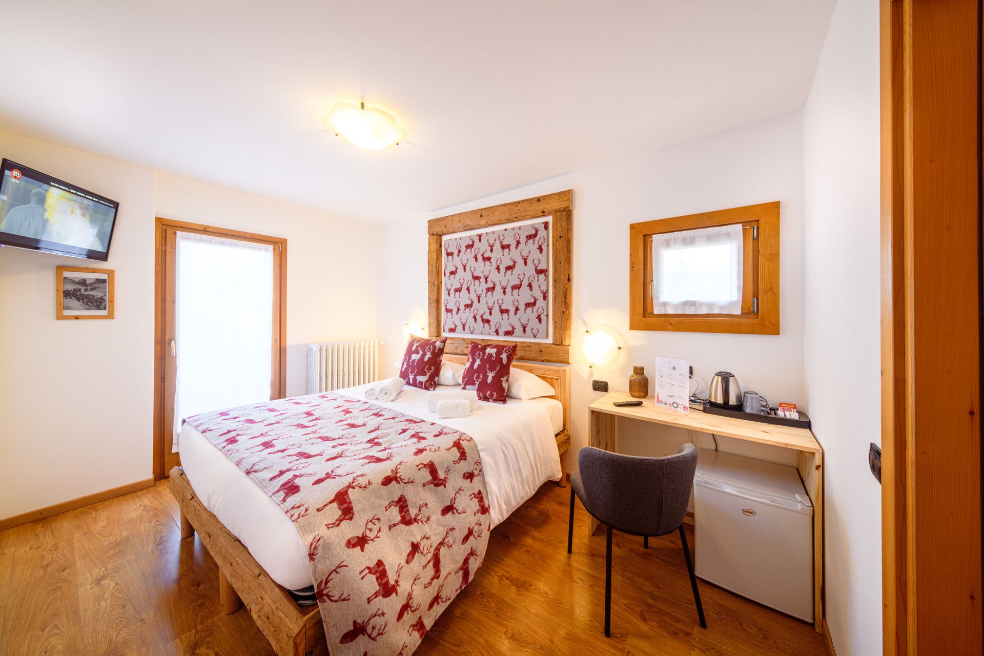 Piccola e luminosa camera da letto con letto, scrivania, specchio e sedia, decorata nei toni del rosso e del bianco.