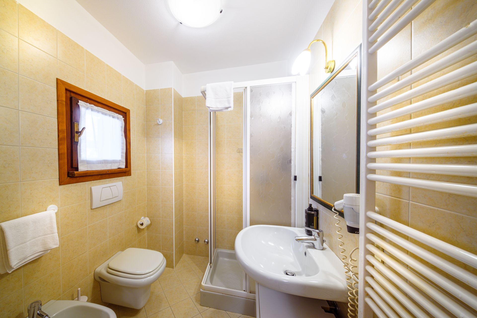Bagno luminoso color beige con doccia, WC, lavabo, specchio e scaldasalviette.