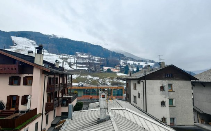 Villaggio alpino innevato con tetti e case sullo sfondo di montagne avvolte dalle nuvole.