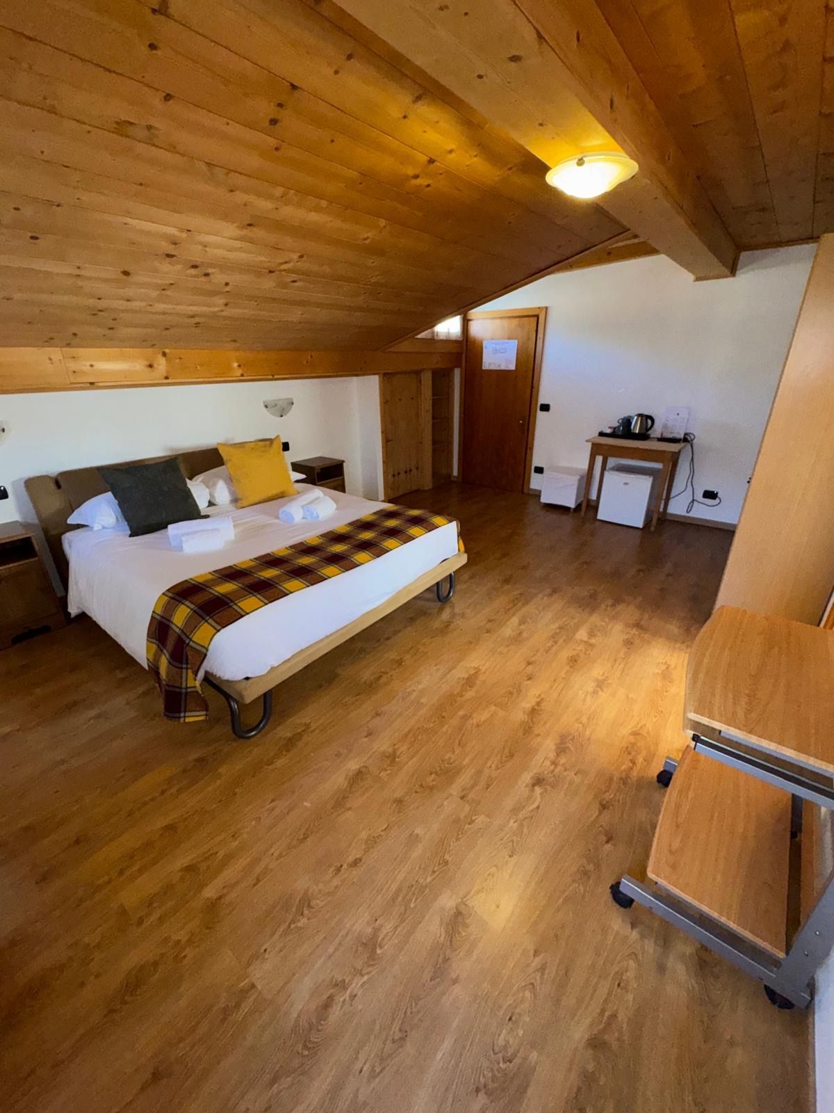 Camera da letto mansardata in legno con soffitto inclinato, letto matrimoniale, scrivania e illuminazione calda.
