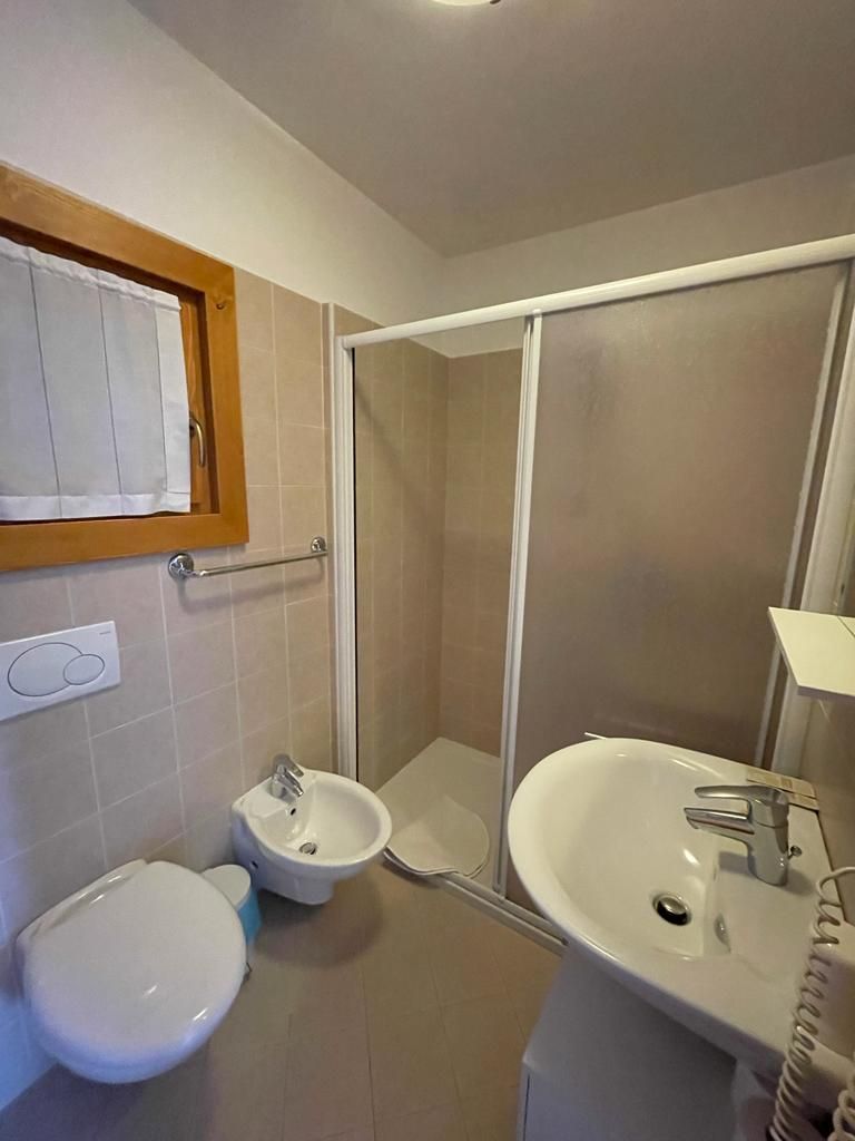 Piccolo bagno con WC, bidet, lavandino e box doccia in vetro.