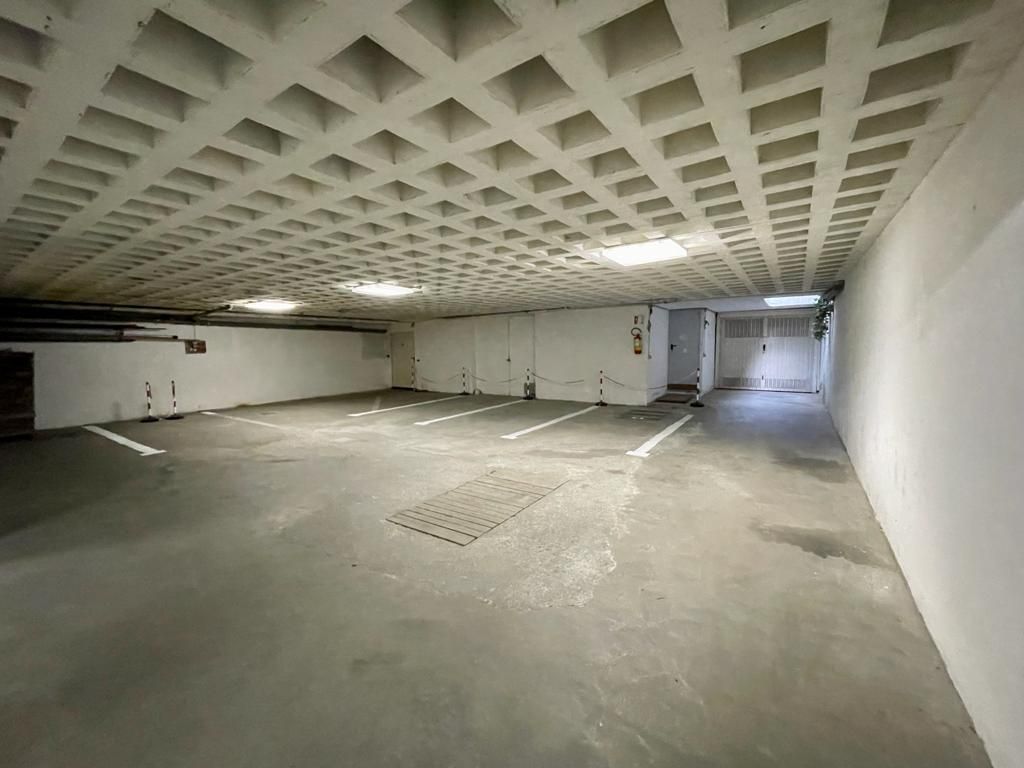 Garage sotterraneo in cemento vuoto con soffitto basso a cassettoni e luce intensa in fondo.