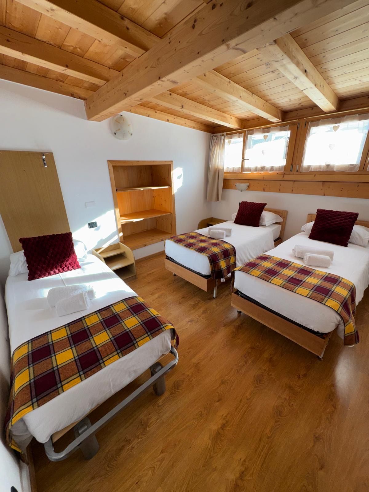 Piccola camera da letto con due letti singoli, soffitto in legno, coperte a quadri e una panca sotto la finestra.