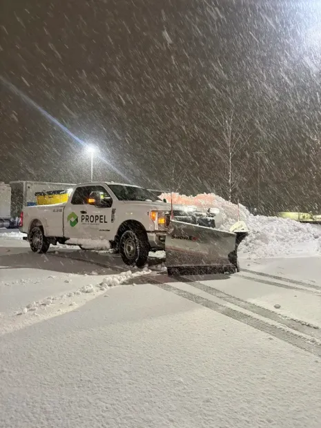 Snowplow truck clearing a snowy road at night during falling snow.