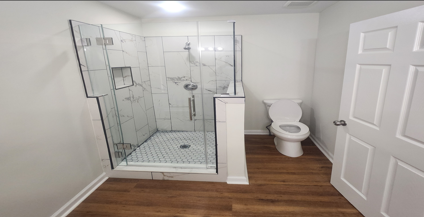Bathroom with glass shower, white toilet, and wood flooring near a white door