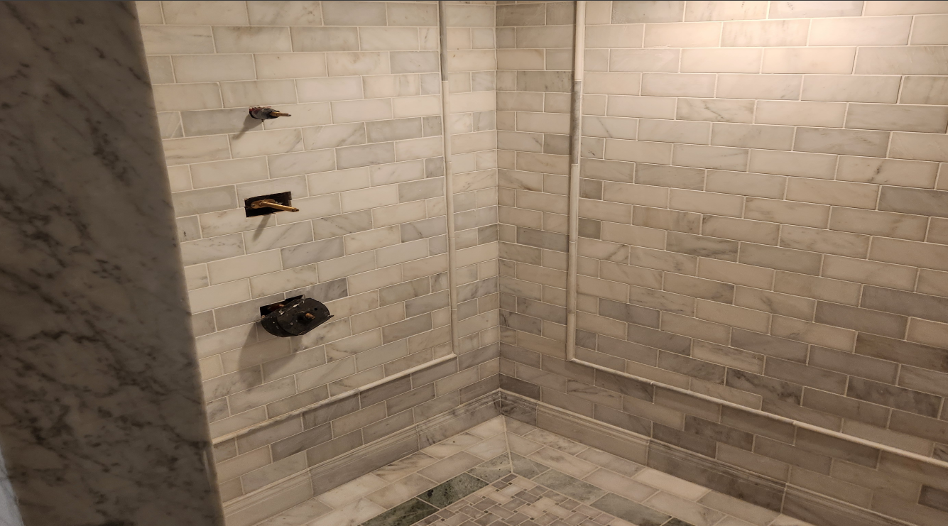 Empty tiled shower stall with beige brick-pattern walls and built-in plumbing fixtures.