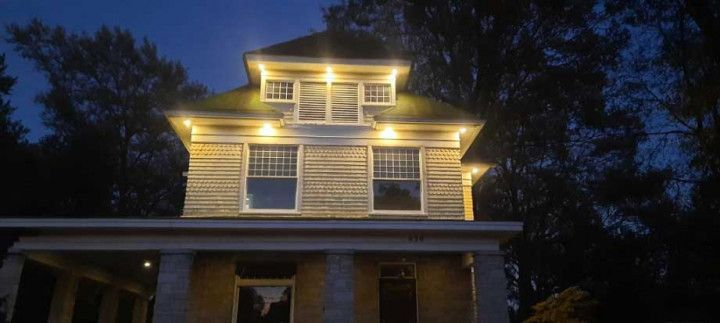 Nighttime view of a lit white house with illuminated upper windows and porch against a dark sky