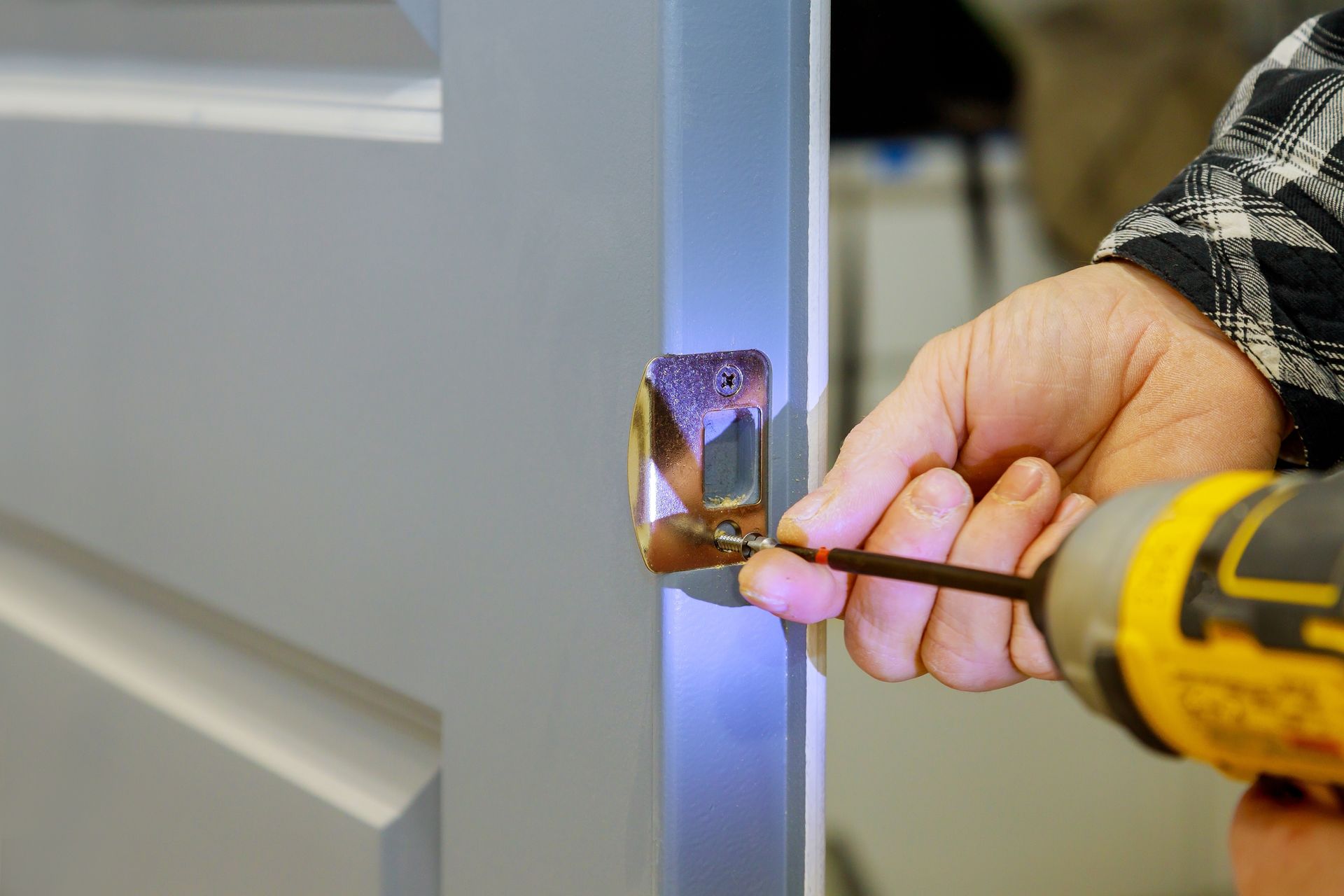 Person using a power drill to install a metal door handle on a white door.
