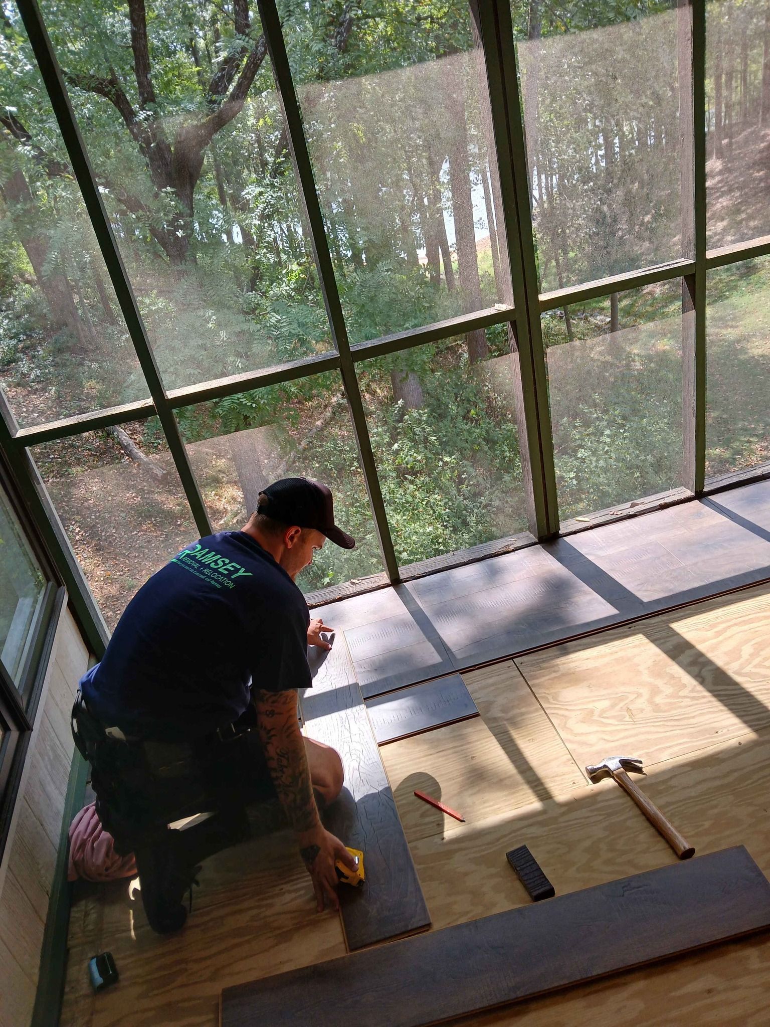 A man is measuring a piece of wood in a screened in porch.