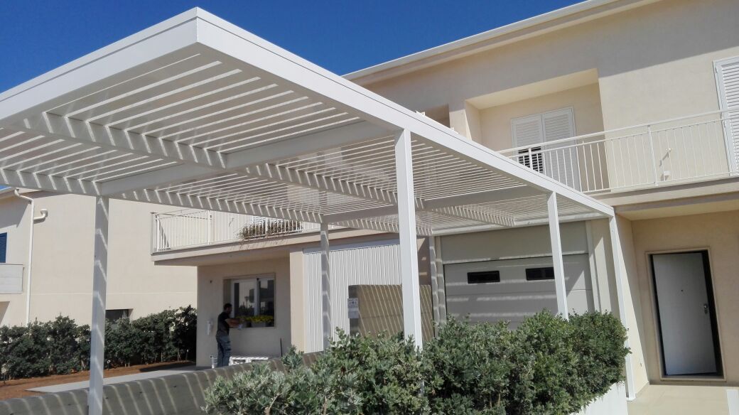 Pergola bianca sopra un patio accanto a una casa beige a due piani con ringhiere bianche e garage.