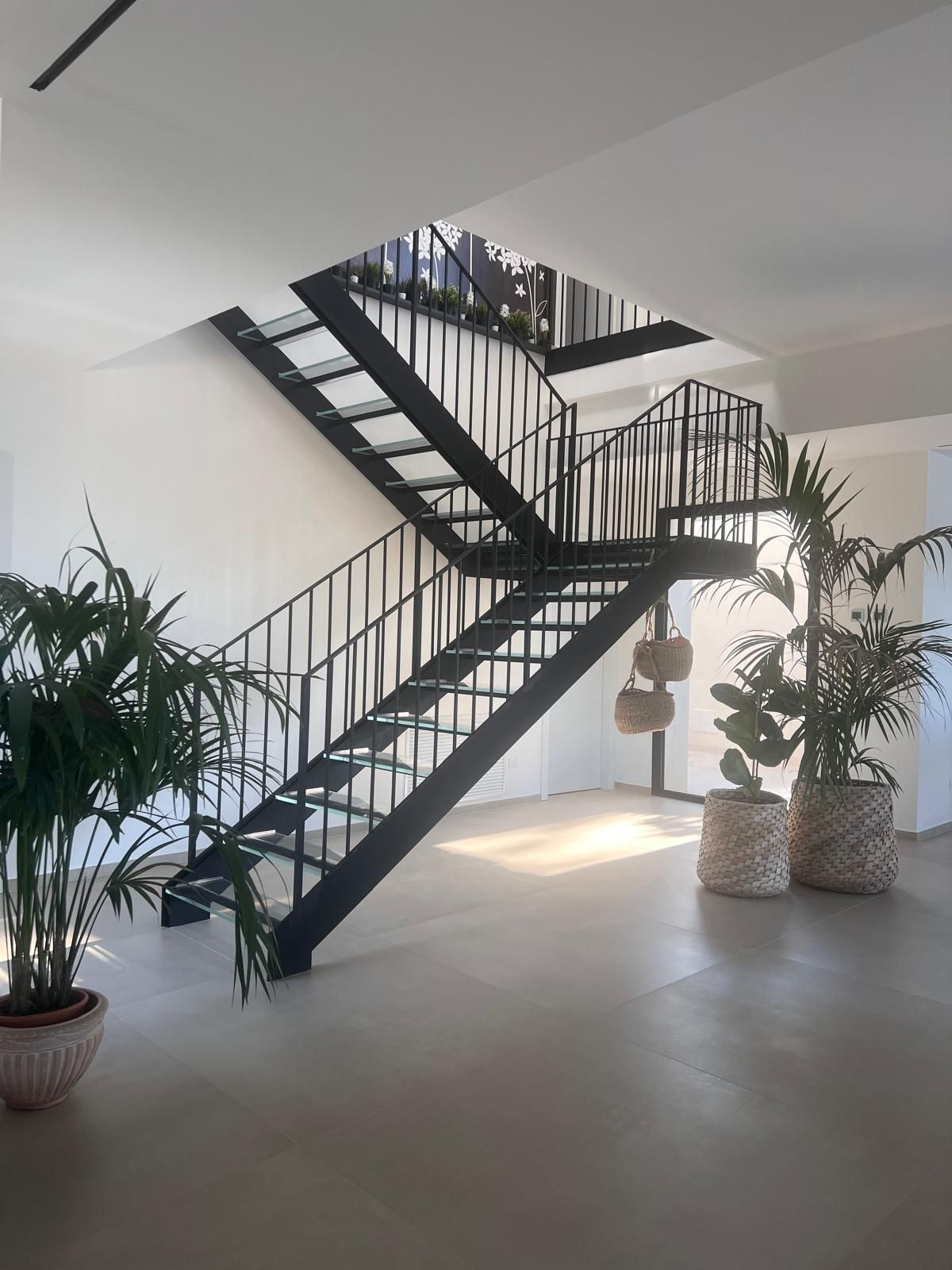 Scala interna moderna con ringhiere nere, pareti bianche e piante in vaso in uno spazio luminoso e minimalista.