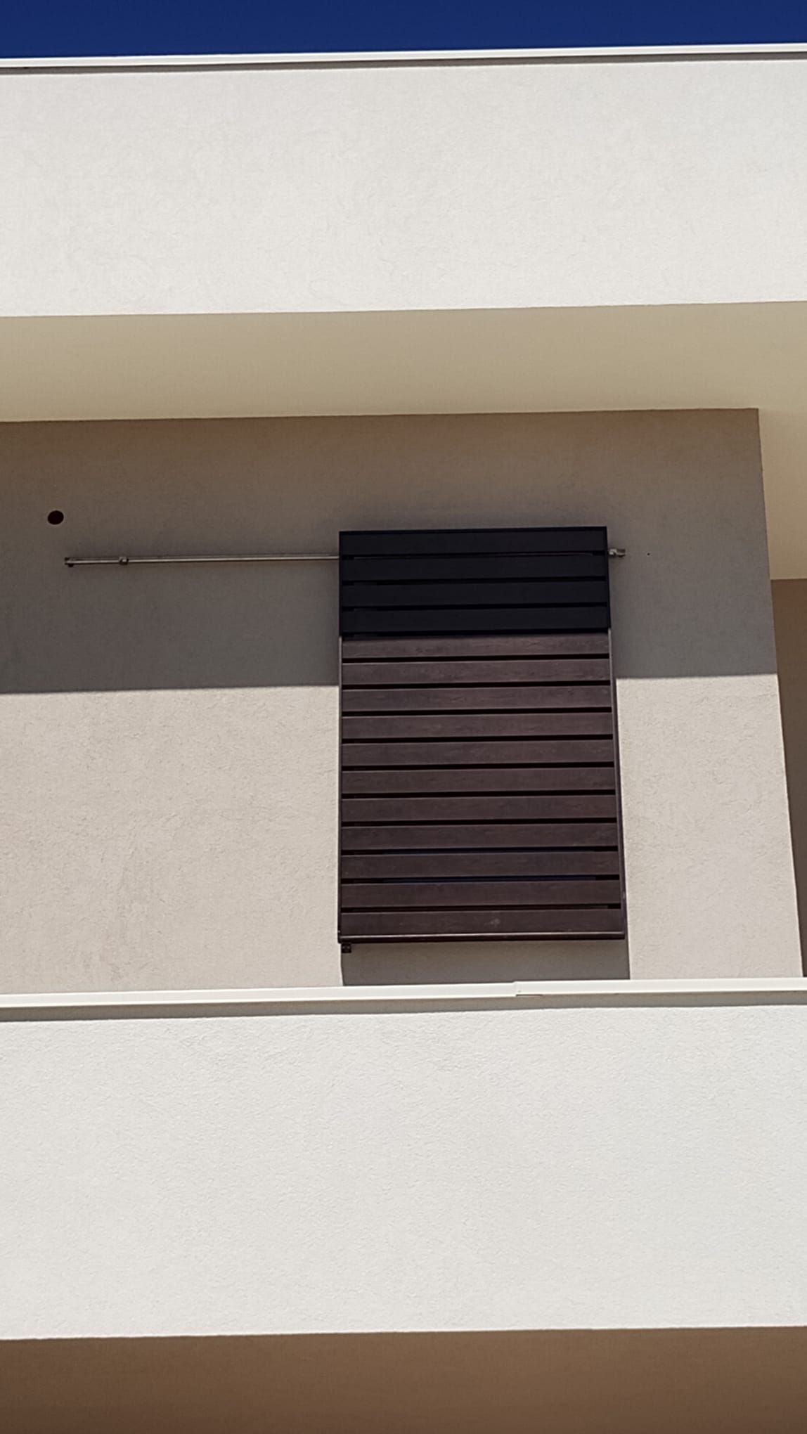 Facciata bianca dell'edificio con un piccolo balcone incassato e una persiana chiusa di colore marrone scuro.