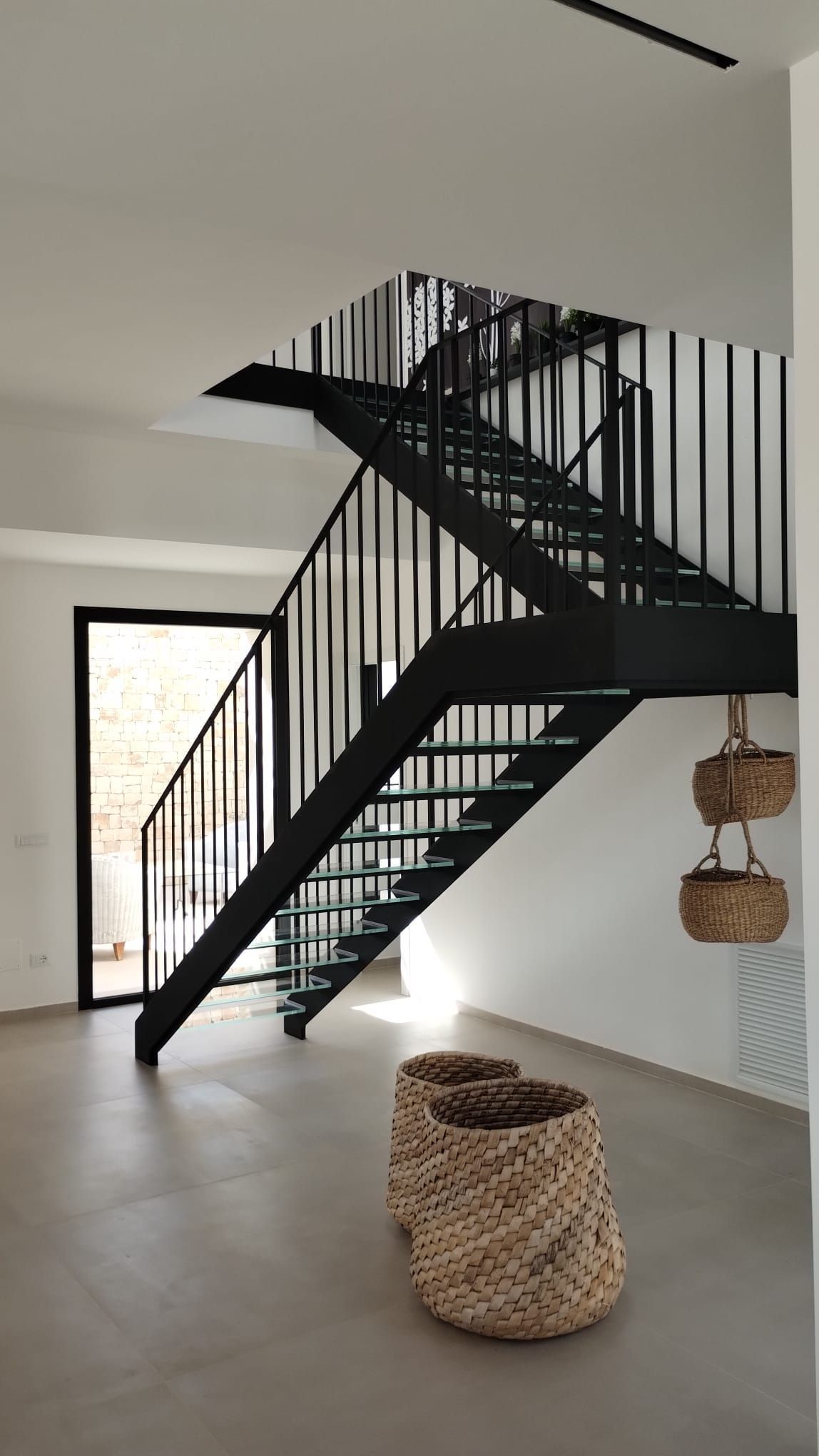 Interno moderno con scala nera, cesto intrecciato e sedie sospese in una stanza luminosa.
